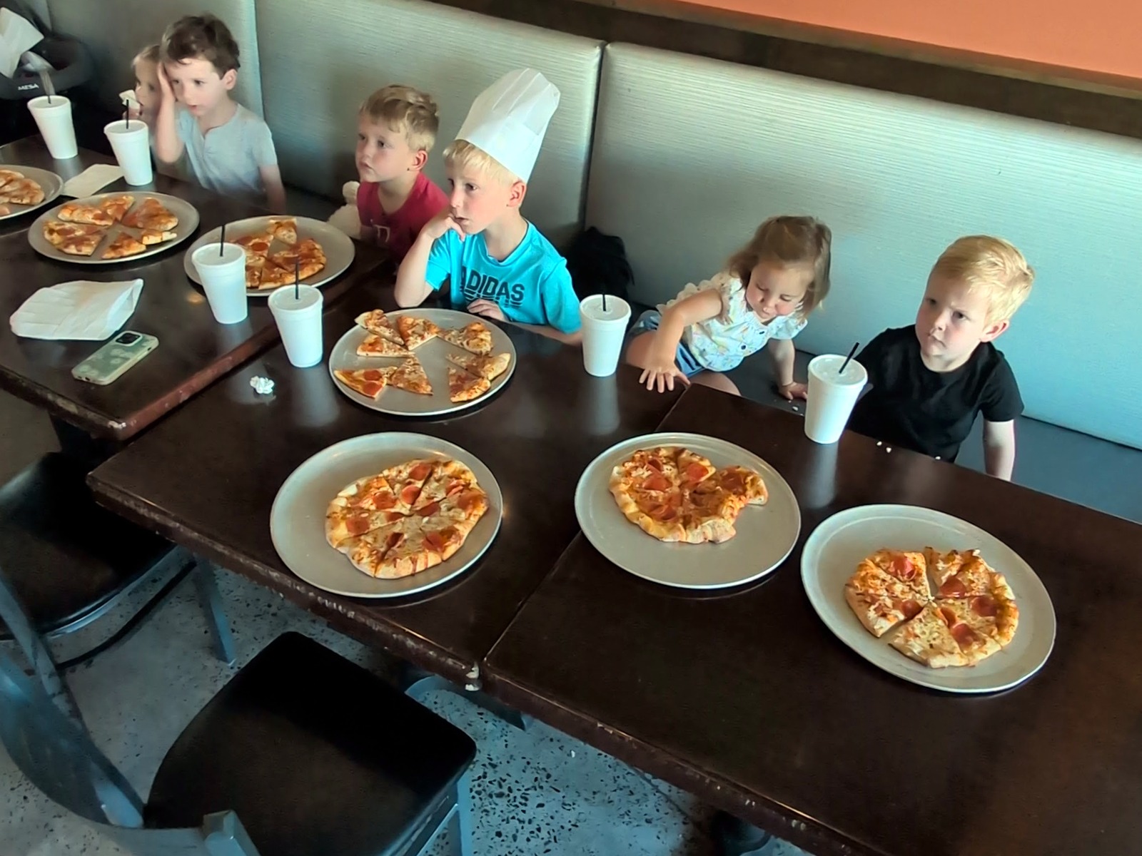 Children in chef hats sitting at a table with finished personal pizzas during a Ruckus kids pizza-making class.