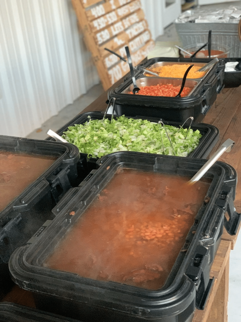A wedding buffet with steaming trays of Tex-Mex staples like beans, shredded lettuce, and toppings.