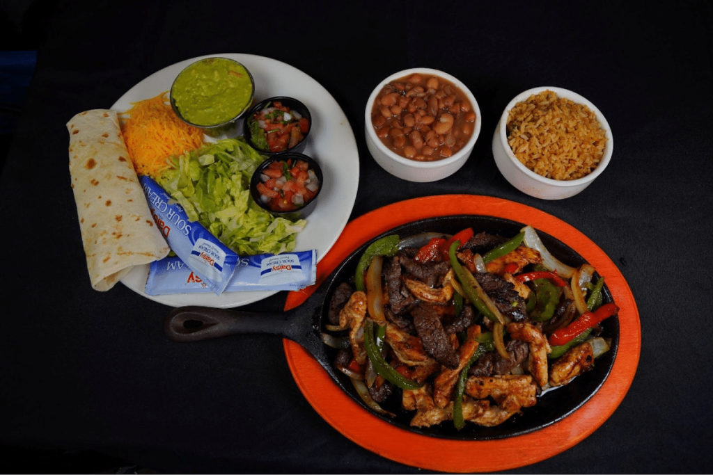 A sizzling Tex-Mex fajita platter with sides of guacamole, lettuce, and beans.