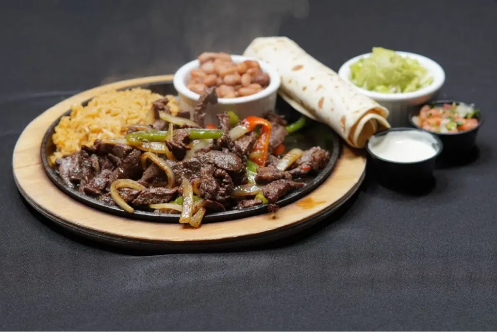 Sizzling beef fajitas with rice, beans, tortillas, and sides.