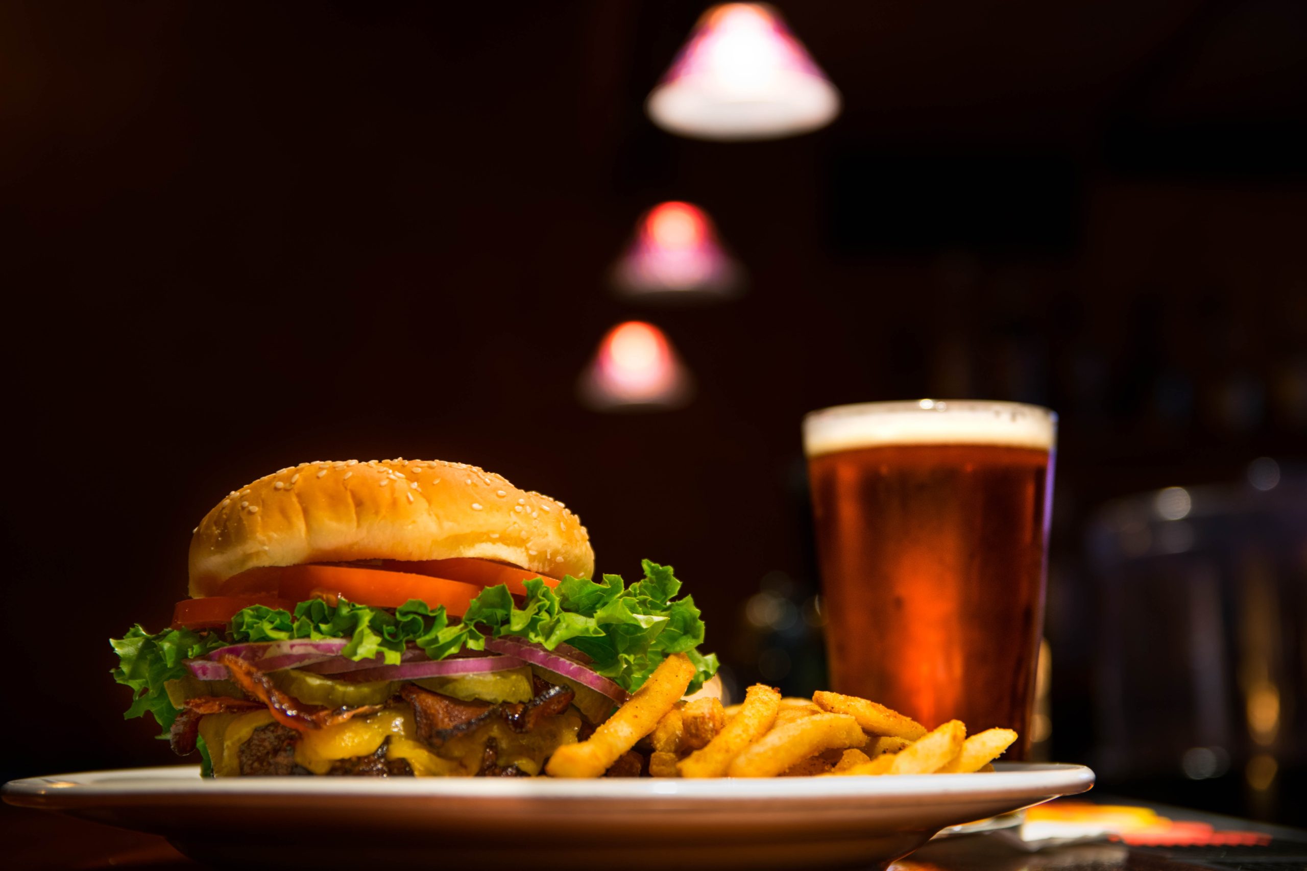 a burger plated with fries next to a beer.